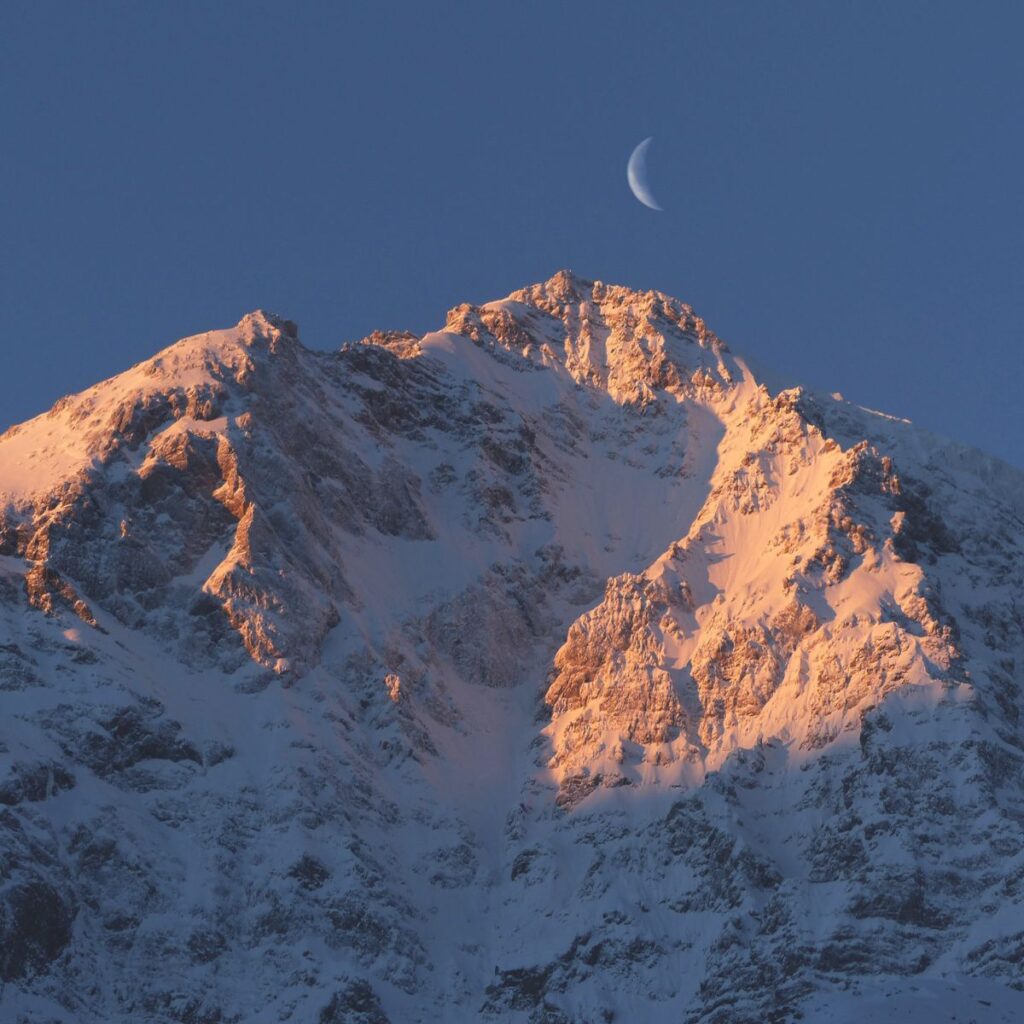 Una montagna innevata e luna visibile nel momento dell'alba